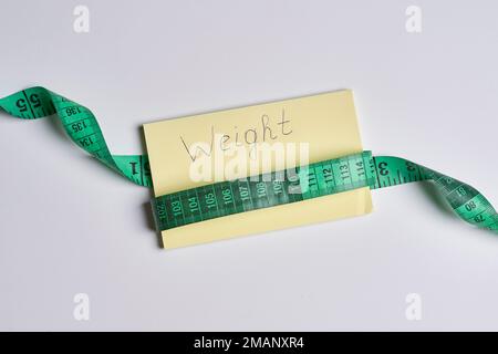 a tape wrapped around a piece of yellow paper with the word weight written on it in black text that reads weight Stock Photo