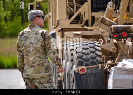 A U.S. Soldier with the 64th Brigade Support Battalion, 3rd Armored Brigade Combat Team, 4th Infantry Division, signals to lower a flat rack from a palatalized load system in preparation to execute resupply operations, Drawsko Pomorskie, Poland, May 31, 2022. The 3/4th ABCT is among other units assigned to V Corps, America’s forward deployed corps in Europe that works alongside NATO allies and regional security partners to provide combat-credible forces. Stock Photo
