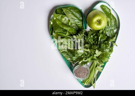 an apple and some greens in a heart shaped container on a white background with space for your text or image Stock Photo