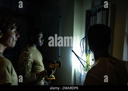 U.S. Air Force Staff Sgt. Sterlin Perkins (center) from the 379th Expeditionary Civil Engineer Squadron, Al Udeid Air Base, Qatar, inspects a breaker box in preparation for adding more power to a building June 3, 2022. The inspection helped these Airmen asses power routing pathways to the areas in the building most in need. 379AEW,AFCENT,Airforce,CivilEngineer,aircombatcommand,usccentcom, Stock Photo