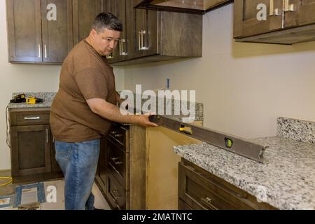 In order to level new kitchen cabinets furniture set during installation, worker hangs level Stock Photo