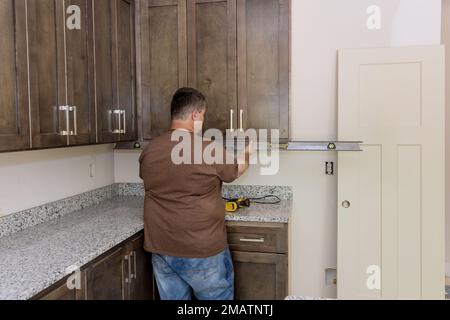In order to level out installation of brand new kitchen cabinets furniture sets worker hangs level Stock Photo