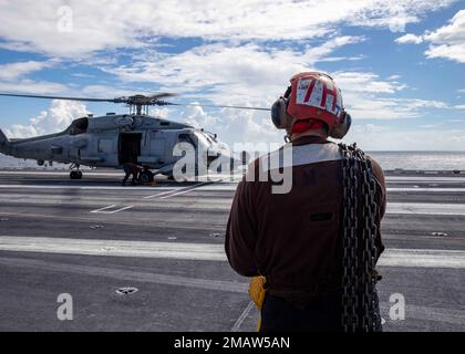 220605-N-OL632-1081 ATLANTIC OCEAN (June 5, 2022) A Sailor assigned to Helicopter Maritime Strike Squadron (HSM) 46, stands by as an MH-60R Sea Hawk helicopter prepares to take off from the flight deck of the aircraft carrier USS George H.W. Bush (CVN 77) during a straits transit training event, June 5, 2022. The George H.W. Bush Carrier Strike Group (CSG) is underway completing a certification exercise to increase U.S. and allied interoperability and warfighting capability before a future deployment. The George H.W. Bush CSG is an integrated combat weapons system that delivers superior combat Stock Photo