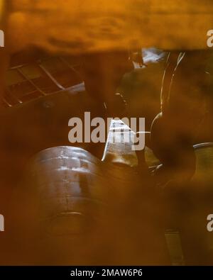 Seen through the reflection of hydraulic fluid on a drain pan, two 5th Aircraft Maintenance Squadron Airmen perform upkeep on a B-52H Stratofortress on June 6, 2022, at Minot Air Force Base, North Dakota. The B-52H can carry and employ a large array of weapons, including gravity bombs, cluster bombs, precision-guided missiles, and joint direct attack munitions. 5th Aircraft Maintenance Squadron,AFGSC,B-52,Minot AFB,U.S. Air Force, Stock Photo