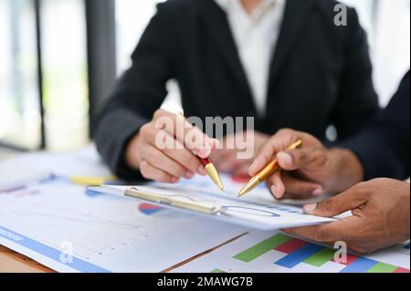 A group of professional businesspeople or financial analysts pointing pen on the report, discussing and analyzing financial data together. cropped ima Stock Photo