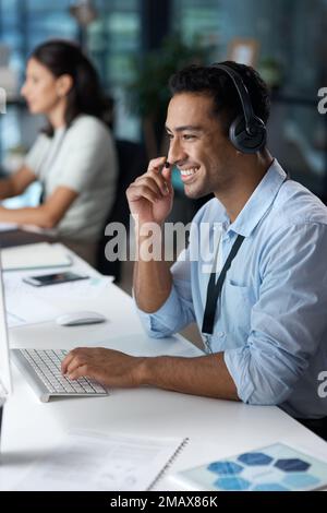 Im so glad you asked. a young man using a headset and computer in a modern office. Stock Photo