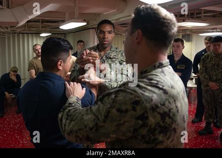 220608-N-IL330-1035 SASEBO, Japan (June 08, 2022) – Master-at-Arms 2nd Class Thomas Bostic, from New York, instructs Sailors on takedown procedures during a security reaction force class in the troop training classroom aboard amphibious assault carrier USS Tripoli (LHA 7), June 8, 2022. Tripoli is operating in the U.S. 7th Fleet area of operations to enhance interoperability with allies and partners and serve as a ready response force to defend peace and maintain stability in the Indo-Pacific region. Stock Photo