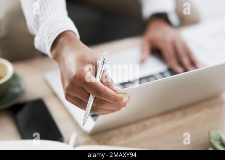 Taking notes with pen to paper and keyboard to computer. Closeup shot of an unrecognisable businessman using a laptop in an office. Stock Photo