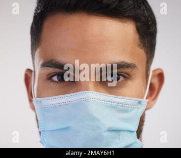Never leave the house without your mask. a handsome young nurse standing alone in the studio and wearing a face mask. Stock Photo