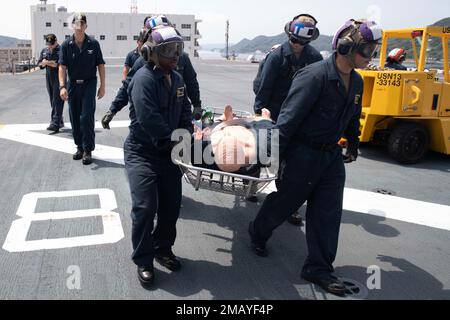 220609-N-IL330-1233 SASEBO, Japan (June 9, 2022) – Sailors carry a simulated casualty during a flight deck firefighting drill aboard amphibious assault carrier USS Tripoli (LHA 7), June 9, 2022. Tripoli is operating in the U.S. 7th Fleet area of operations to enhance interoperability with allies and partners and serve as a ready response force to defend peace and maintain stability in the Indo-Pacific region. Stock Photo