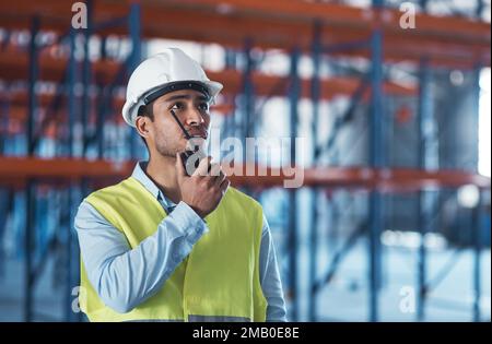 Im looking right at the shipment. a handsome young contractor standing alone in the warehouse and using a walkie talkie. Stock Photo
