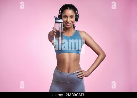 Keep yourself hydrated. Cropped portrait of an attractive and sporty young woman wearing headphones and posing with a water bottle in studio against a Stock Photo