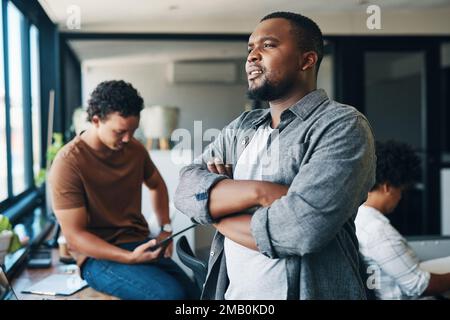 It seems like a really nice day to be outside. a young businessman with his arms crossed in an office. Stock Photo