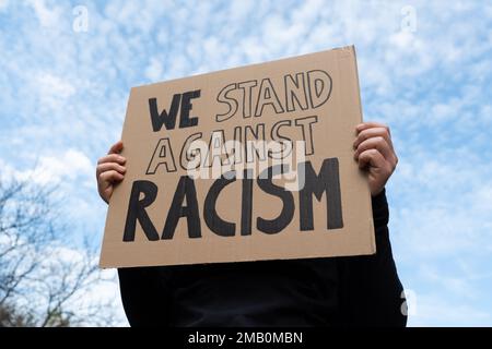 Girl holding a cardboard banner sign with slogan We Stand Against Racism. Woman with placard at Black Lives Matter protest rally demonstration. Stock Photo
