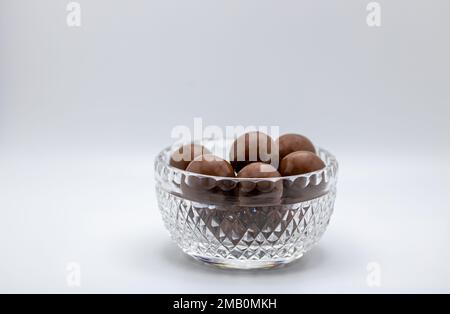 Macro view of a small beautiful vintage lead crystal bowl containing round malted chocolate candies, on white background with copy space Stock Photo