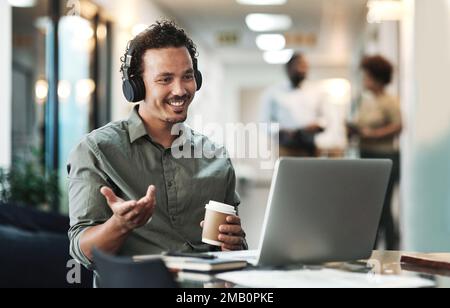 Virtual meetings are the way forward. a young businessman sitting in the office and wearing headphones while using his laptop for a virtual meeting. Stock Photo