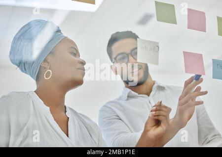 So, heres the plan...two diverse young businesspeople working on a glass wipe board in the boardroom. Stock Photo