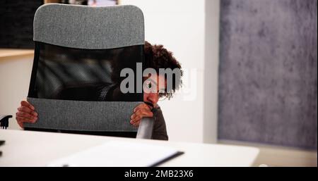 Scared Man Hiding Behind Office Desk In Room Stock Photo