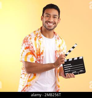 Portrait, clapper board and man in studio isolated on a yellow background. Director, film production and happy male model in stylish or cool tie dye Stock Photo