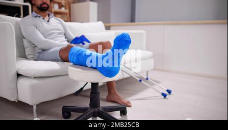 Young Man With Broken Leg Sitting On Sofa Stock Photo