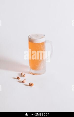 Chilled beer mug with frost on the surface and foam inside on a white background, Pistachios Stock Photo