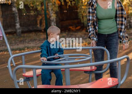 A boy, person with down syndrome walks in the park with his mother, spinning on the carousel Stock Photo