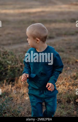 Cute blond Little boy, person with down syndrome walks in the park Stock Photo