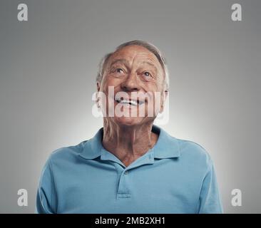 I can see you up there you know. an elderly man smiling while gazing above himself in a studio against a grey background. Stock Photo