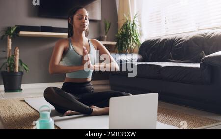 meditation is a great way to start your day. a young woman following a yoga routine using her laptop at home. Stock Photo