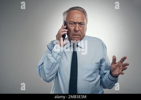 Slow down so I can understand you. a senior businessman standing against a grey background in the studio and looking confused while using his Stock Photo