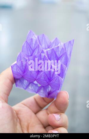 Person holding a abstract model printed on a 3D printer from purple plastic on his hand on gray background close-up. Concept modern printing technology Stock Photo