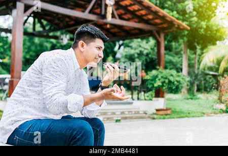 Man sitting sending a voice message with his phone and gesturing with his hands. Handsome man sitting outside sending a voice message with his cell Stock Photo