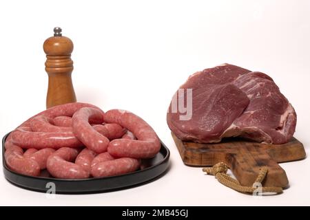 Fresh raw sausages on a black tray and Veal sirloin steak raw on a wooden board isolated on a white background Stock Photo