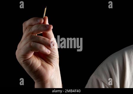A hand holds an unlit match on a black background Stock Photo