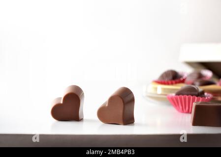 Heart shaped chocolates on white table and box of chocolates on white isolated background. Front view. Stock Photo
