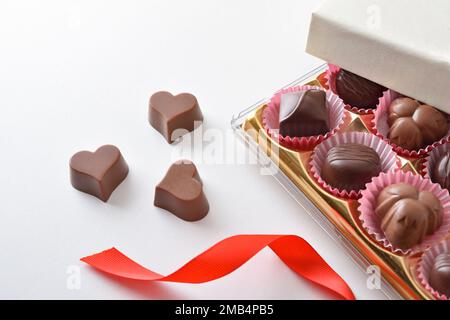 Box with assortment of chocolates on white table for event with red bow. Top elevated view. Stock Photo