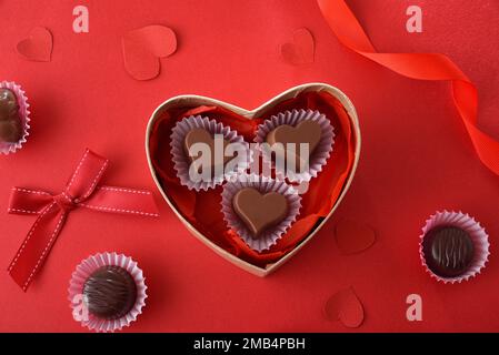 Chocolates in heart shaped box on red table decorated with hearts and red ribbons. Top view. Stock Photo