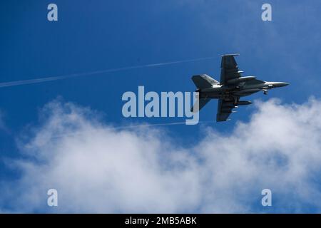 PHILIPPINE SEA (June 12, 2022) An F/A-18E Super Hornet, assigned to the 'Tophatters' of Strike Fighter Squadron (VFA) 14, flies over the Nimitz-class aircraft carrier USS Abraham Lincoln (CVN 72). Abraham Lincoln Strike Group is on a scheduled deployment in the U.S. 7th Fleet area of operations to enhance interoperability through alliances and partnerships while serving as a ready-response force in support of a free and open Indo-Pacific region. Stock Photo