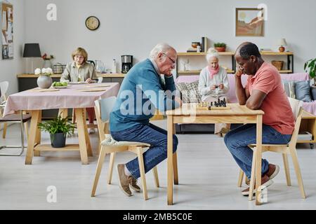Group of senior people spending time in nursing home, they playing chess, knitting and reading books Stock Photo