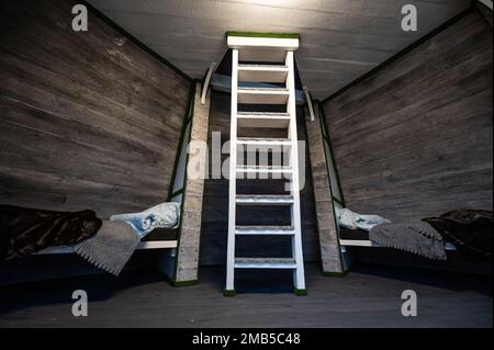 Two single beds with linen mounted in niches of a room. Pyramid shape bungalow summer house. Angled surrounded walls, white stairs, gray horizontal wo Stock Photo
