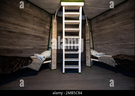 Two single beds with linen mounted in niches of a room. Pyramid shape bungalow summer house. Angled surrounded walls, white stairs, gray horizontal wo Stock Photo
