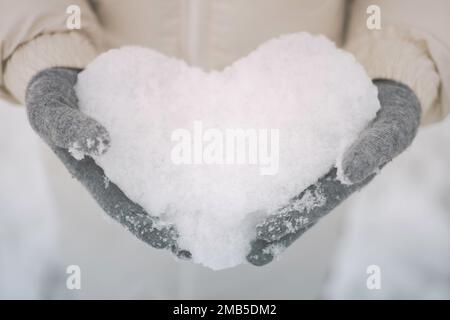 Closeup female hands in woolen gloves holding snowy heart shape love winter day Stock Photo