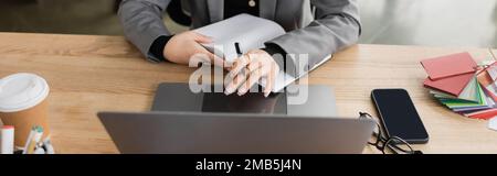 Cropped view of designer with notebook using laptop in studio, banner,stock image Stock Photo