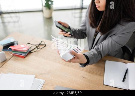 Cropped view of interior designer using smartphone and holding color samples in office,stock image Stock Photo