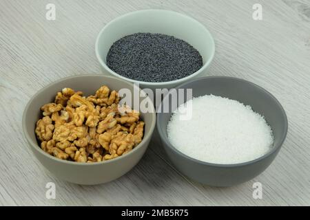 Ingredients for adding to baking. Poppy seeds, coconut shavings and walnut in bowls on a woody background. Vegetarian product. Stock Photo