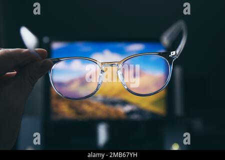 Selective focus on transparent clear blue light computer glasses and computer screen glowing on the background in home or office. Blue light glasses. Stock Photo