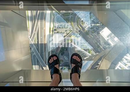 Tourists posing on a glass floor in a skyscraper. feet on the glass floor of a high skyscraper, a dangerous scary look. Stock Photo