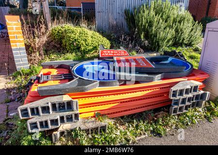 A pile of roadwork signs and barriers discarded on a grass verge at the side of a road ready to collect. Stock Photo