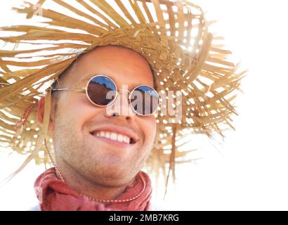 Dressed for summer fun. a young man wearing sunglasses and a straw hat smiling. Stock Photo