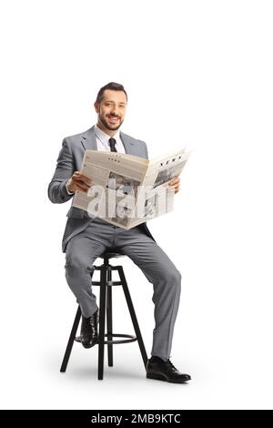 Young professional man in a suit sitting on a chair with a newspaper and smiling at camera isolated on white background Stock Photo